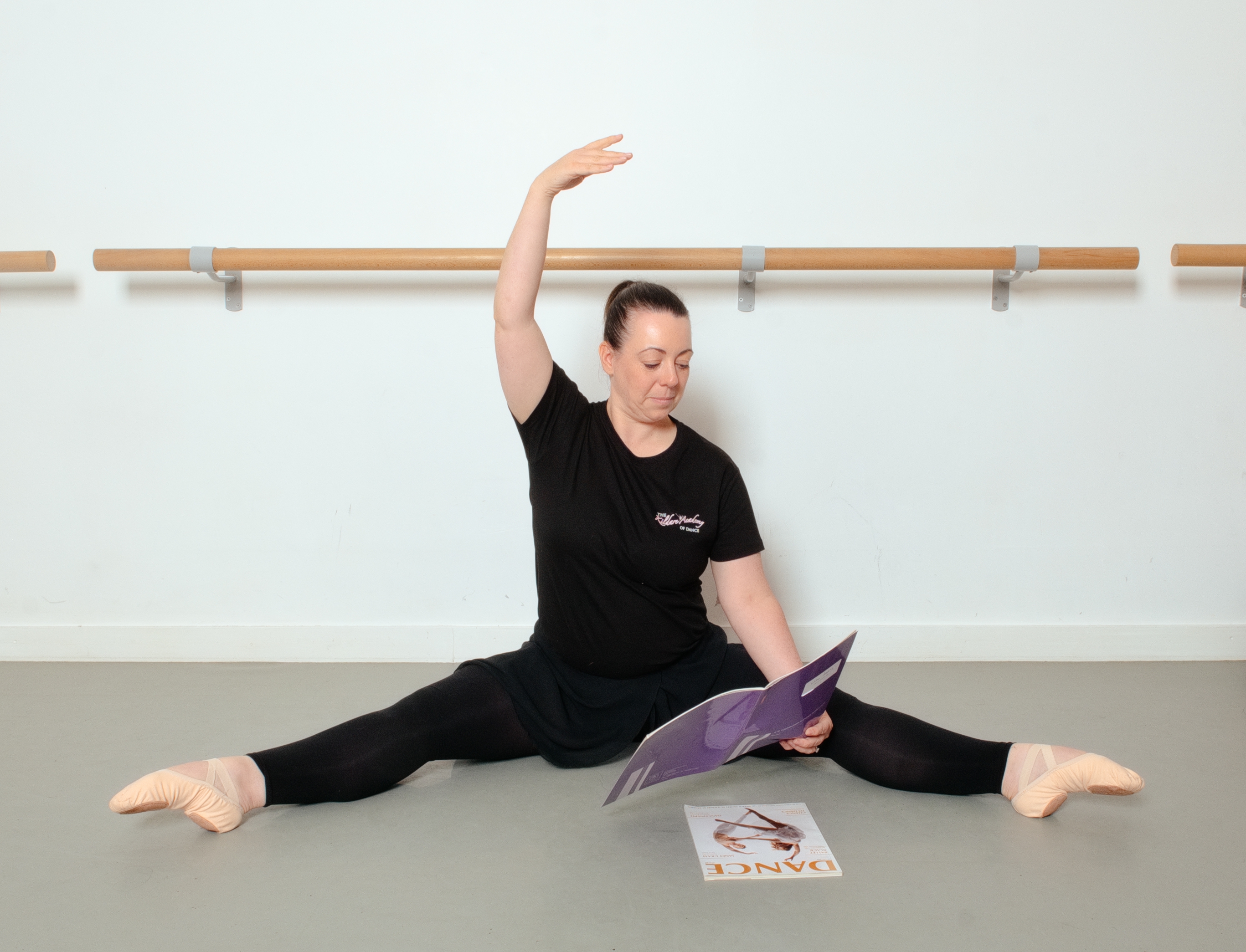 Dance tutor practising an arm position while consulting course material